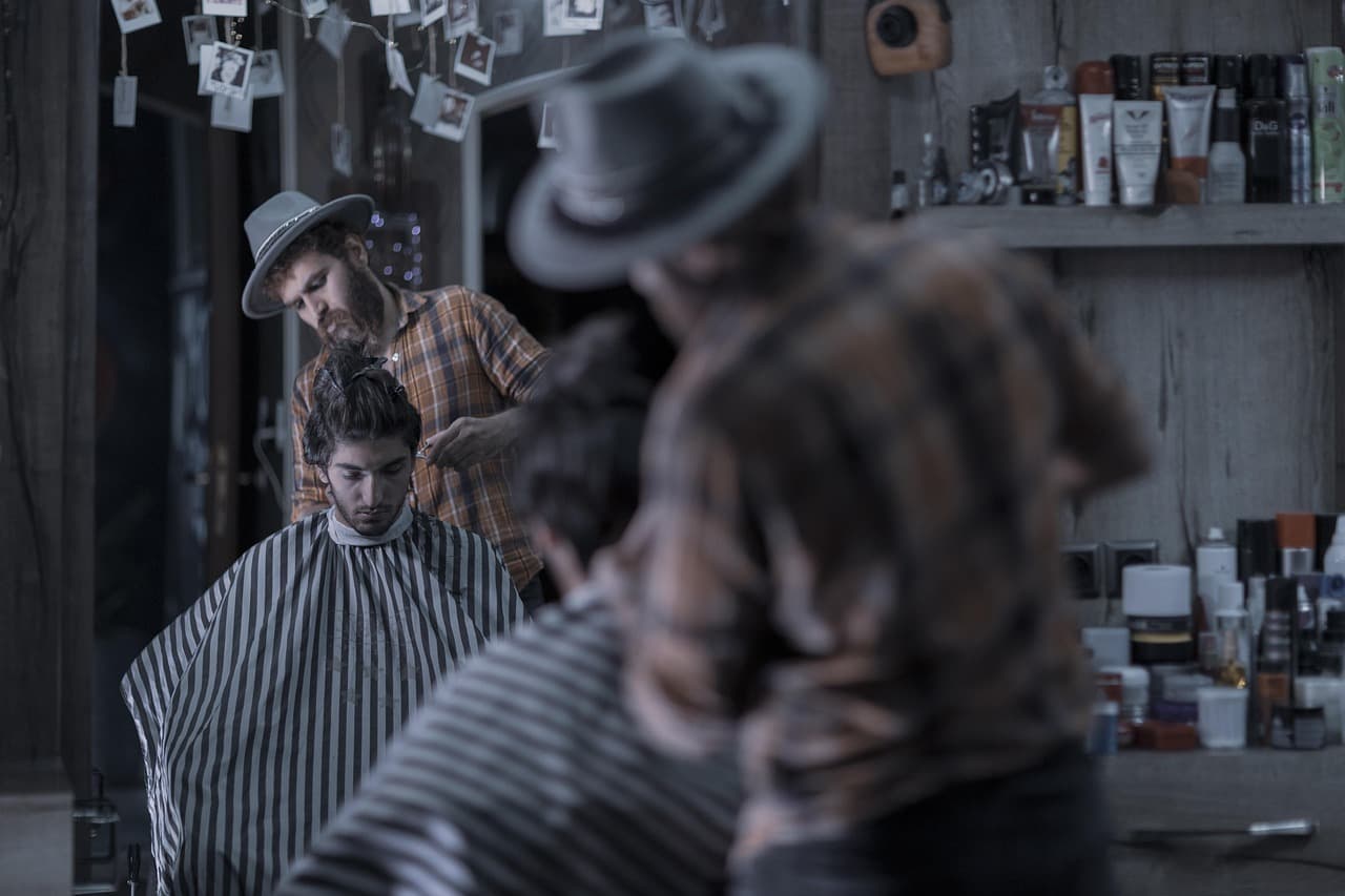 A barber at work in a low-lit shop, seen past another barber in the foreground